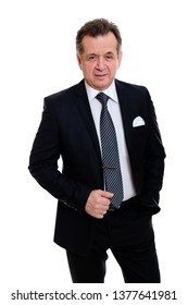 Portrait Of Handsome Confident Caucasian Mature Businessman 55-60 Years Old In Black Suit Standing With Hand In Pockets Smiling In Front On Isolated White Background.