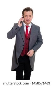 Portrait Of Handsome Confident Caucasian Mature Businessman 55-60 Years Old In Grey Tuxedo And Red Vest. Rich Senior Man Talk By Phone And Looking To Camera On Isolated White Background