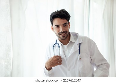 Portrait of a handsome, confident male doctor standing in the clinic. dressed in a doctor's uniform have headphones over the neck happy smile a doctor who specializes in treating patients