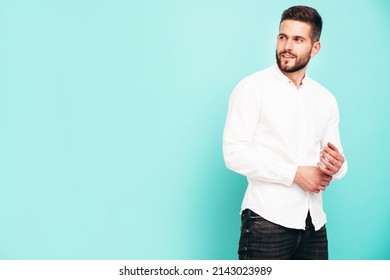 Portrait Of Handsome Confident  Model. Sexy Stylish Man Dressed In White Shirt And Jeans. Fashion Hipster Male Posing Near Blue Wall In Studio. Isolated