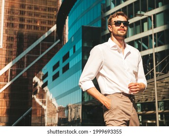 Portrait of handsome confident stylish hipster lambersexual model.Modern man dressed in white shirt. Fashion male posing in the street background near skyscrapers in sunglasses. Outdoors at sunset  - Shutterstock ID 1999693355