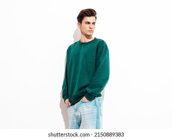 Portrait of handsome confident stylish hipster lambersexual model.Man dressed in green sweater and jeans. Fashion male posing in studio near white wall. Isolated