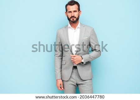 Portrait of handsome confident stylish hipster lambersexual model.Sexy modern man dressed in elegant suit. Fashion male posing in studio near blue wall. Looking at camera