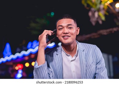 Portrait Of A Handsome And Dapper Young Man Hanging Out At An Outdoor Bar. Holding A Phone Listening To Someone. Nightlife Scene At A Popular Spot.