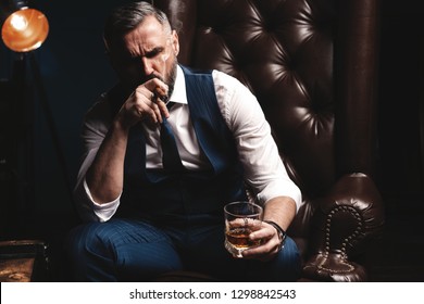 Portrait Of Handsome Elegant Mature Man With Cigar And A Glass Whiskey In A Dark Room