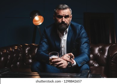 Portrait Of Handsome Elegant Mature Man With Cigar And A Glass Whiskey In A Dark Room