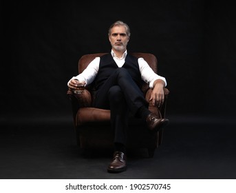 Portrait of handsome elegant mature man with a glass whiskey in a dark room.