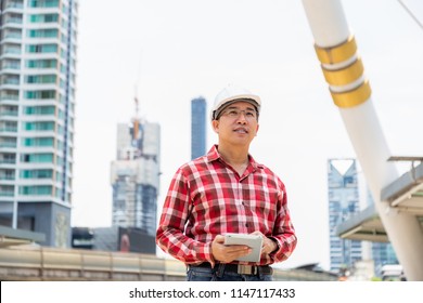 Portrait Handsome Engineer Guy. Attractive Handsome Engineer Man Hold Tablet And Looking At The Construction Of Building. Middle Aged Handsome Man Is A Head Or Boss Of Company. He Feels Happy With Job