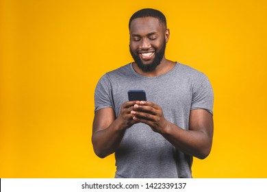 Portrait of handsome excited cheerful joyful delightful curious guy wearing casual sending and getting messages to his lover isolated against yellow background. Using phone. 