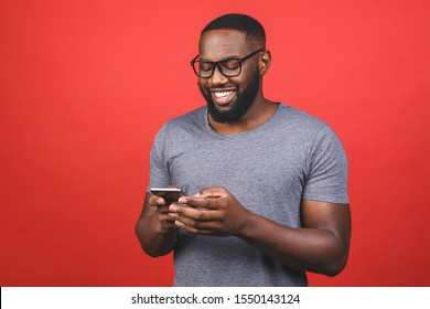 Portrait Of Handsome Excited Cheerful Joyful Delightful African American Guy Wearing Casual Sending And Getting Messages To His Lover Isolated Against Red Background. Using Phone. 