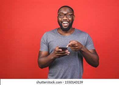 Portrait Of Handsome Excited Cheerful Joyful Delightful African American Guy Wearing Casual Sending And Getting Messages To His Lover Isolated Against Red Background. Using Phone. 