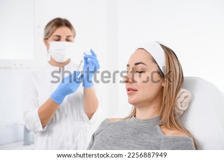 portrait of handsome female patient on couch in beauty clinic and female cosmetologist in blue latex gloves on background. Cosmetology concept.