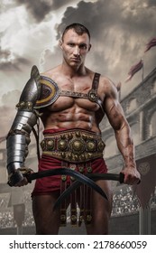 Portrait of handsome gladiator with dual swords dressed in light armor posing in ancient arena.