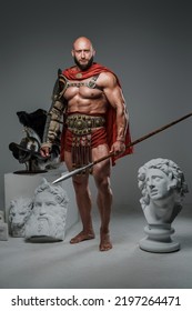 Portrait of handsome gladiator with spear posing around marble greek statues.