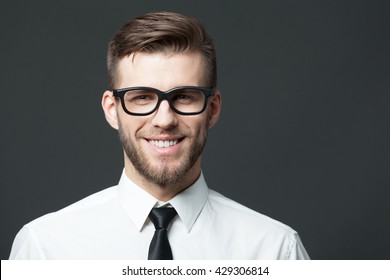 Portrait Of Handsome Happy Young Businessman Standing Against Dark Gray Background.