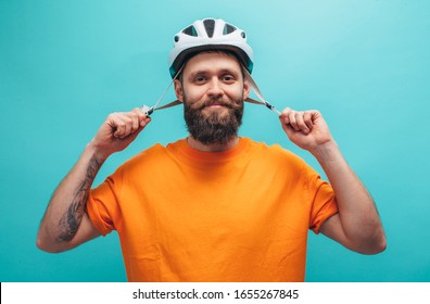 Portrait of handsome hipster guy with beard wearing blank orange t-shirt and white bike helmet, isolated on blue studio wall.