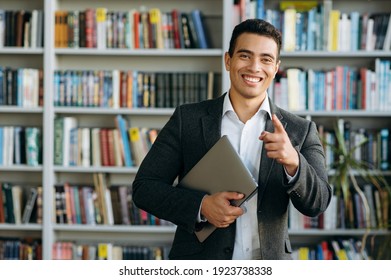 Portrait of handsome hispanic businessman or student in formal stylish suit, holding a laptop in hands and looking directly at the camera with friendly smile