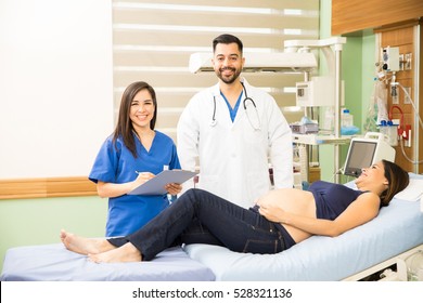 Portrait Of A Handsome Hispanic Doctor And A Pretty Nurse Checking On A Pregnant Woman In A Hospital