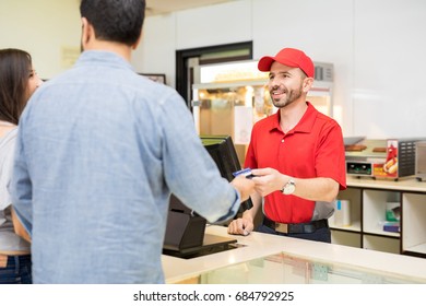 Portrait Of A Handsome Hispanic Man Working In A Concession Stand At A Movie Theater And Selling Snacks To Some Customers