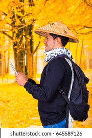 Portrait Of A Handsome Hispanic Young Business Guy Wearing An Asian Conical Hat And Holding His Ipad In His Hands In Autum Background