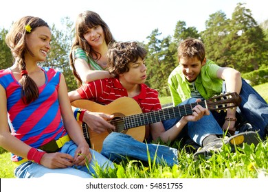 Portrait of handsome lad playing the guitar surrounded by his friends - Powered by Shutterstock