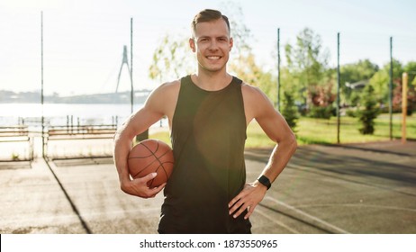 Portrait of handsome male basketball player smiling at camera while posing with a basketball on the court on a sunny day. Sport, active lifestyle concept. Front view. Web Banner - Powered by Shutterstock