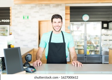 Portrait of handsome male cashier at checkout counter in grocery store