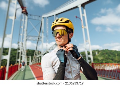 Portrait of a handsome male cyclist in a helmet and sporty outfit on the background of the bridge, looks away with a serious face and wears protection - Shutterstock ID 2136233719