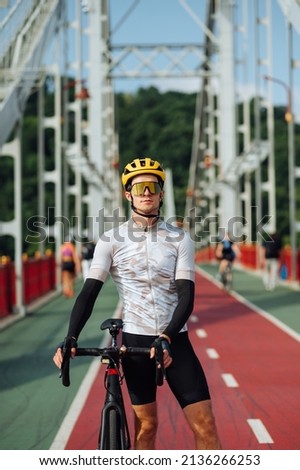 Portrait of handsome male cyclist with cyclist on cityscape background in full outfit posing at camera