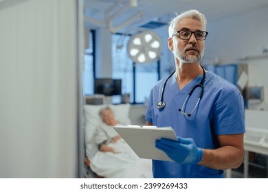 Portrait of handsome male doctor, patient in hospital bed behind. ER doctor examining senior patient, reading her medical test, lab results in clipboard.