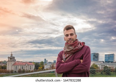 Portrait of handsome man with crossed arms at dramatic sky and urban background. Atractive guy standing at terrace on colorful sky and city backdrop. Urban guy. Powerful and determined man concept. - Powered by Shutterstock