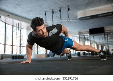 Portrait of a handsome man doing push ups exercise with one hand in fitness gym