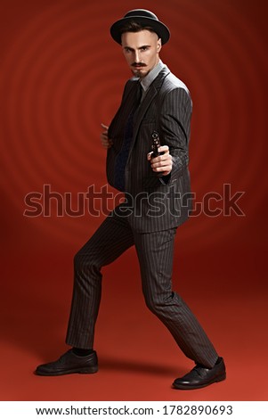 Portrait of a handsome man in elegant classical suit and a hat holding the gun ready, illuminated by circles of light target. Retro style. Criminal world, detective.