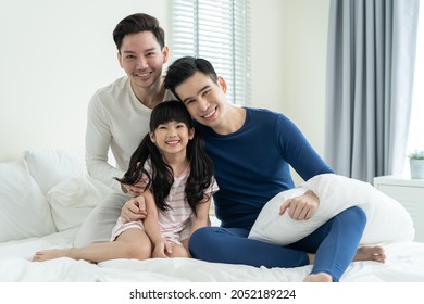 Portrait Of Handsome Man Gay Family With Young Kid Daughter In Bedroom. Attractive Romantic Male Lgbt Couple Sitting On Bed With Little Adorable Girl Child In Early Morning, Enjoy Parenting In House.