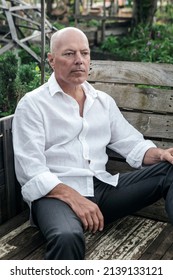 Portrait Of Handsome Man In His 50s Sitting On Bench In Garden