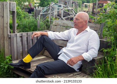 Portrait Of Handsome Man In His 50s Sitting On Bench In Garden