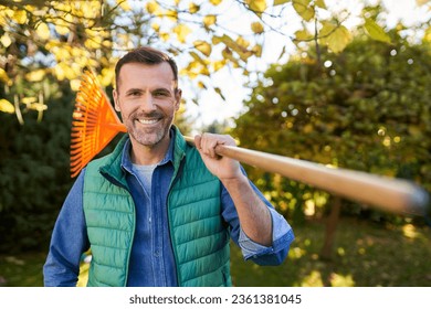 Portrait of handsome man holding leaf rake during autumn cleanup in garden - Powered by Shutterstock