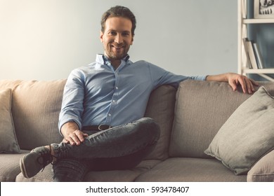 Portrait Of Handsome Man Looking At Camera And Smiling While Sitting On Couch At Home