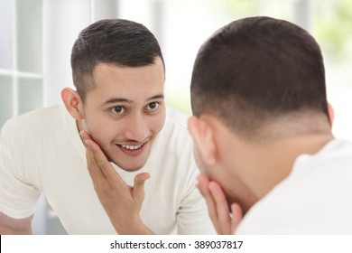 Portrait Of Handsome Man Looking Into The Mirror And Touching His Smooth Face