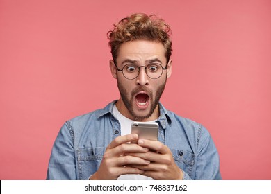Portrait of handsome man looks shocked in smart phone, sees calendar date, finds out that he can`t manage to go on meeting, types message of refusal. People, emotions and technology concept.