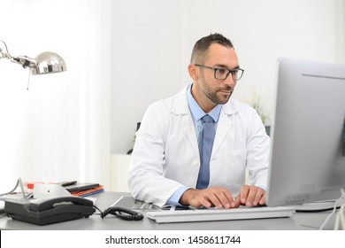 Portrait Of A Handsome Man Male Doctor In Medical Practice Office Working On Computer