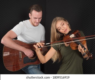 Portrait of a handsome man musician plays the guitar, a beautiful woman musician plays the violin in the recording studio. - Powered by Shutterstock