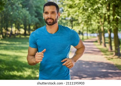 Portrait Of Handsome Man Running In A Park With Earphones During Summer