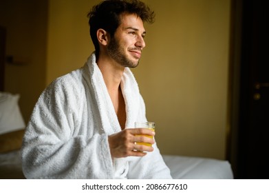 Portrait Of A Handsome Man In White Bathrobe Drinking Orange Juice In A Hotel Suite