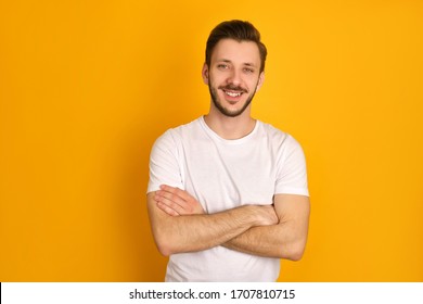 A portrait of handsome man in in white t-shirt crossing hands over yellow background, smiling happily, feeling attractive.
