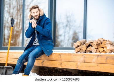 Portrait Of A Handsome Man In Winter Clothes Filling Cold Sitting On The Terrace Of The Modern House