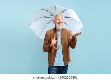 Portrait of handsome mature bearded man wearing stylish brown jacket holding umbrella looking away isolated on blue background. Protection concept, weather forecast - Powered by Shutterstock