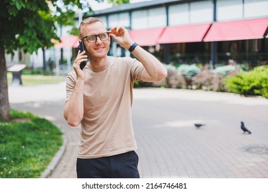 Portrait of handsome mature businessman holding messenger bag, wearing stylish eyeglasses looking at camera. Smiling middle aged man using smartphone, standing on the street. Mobile banking concept