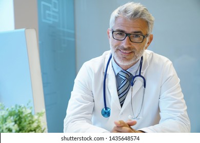 Portrait Of Handsome Mature Doctor Sitting At Desk In Modern Office