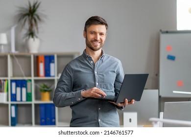 Portrait Of Handsome Mature Male Office Worker With Laptop In Hands Standing In Office And Smiling At Camera, Middle Aged Male Holding Computer Near Workplace